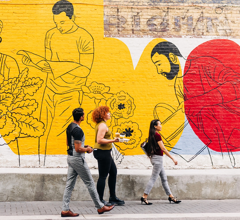 Friends walking by mural with coffee